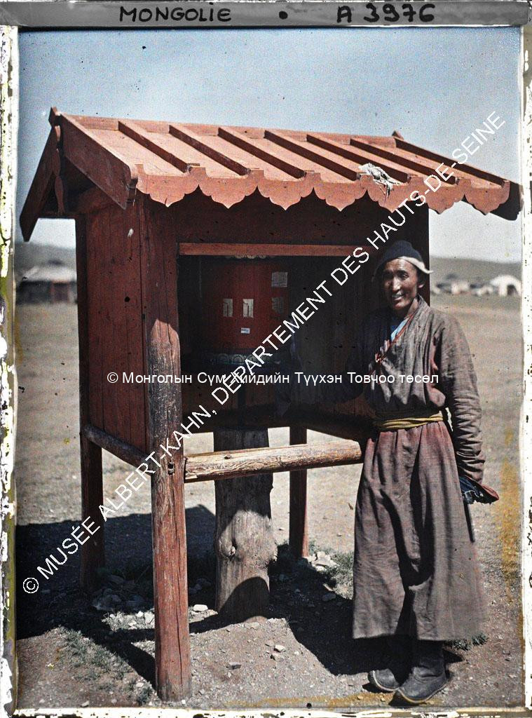 A monk in front of a prayer wheel behind Gandan (?). Musée Albert-Kahn. A 3976. Photo by Stéphane Passet, 23 July 1913